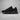 New Balance black chunky sneaker side profile on grey textured studio background with soft lighting