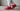 Nike Shox R4 Red White sneakers on foot with grey joggers and white crew socks in a clean industrial lifestyle setting.